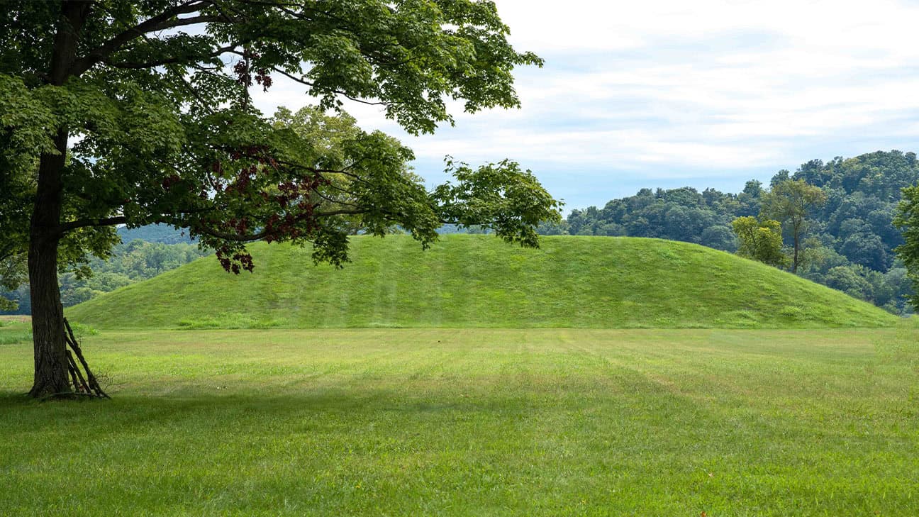 A mound with a tree to the left featured at the Spiro Mounds Center.