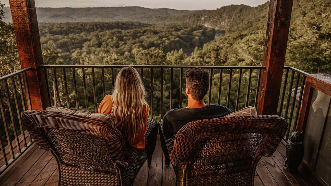A couple sitting at a cabin, overlooking trees.