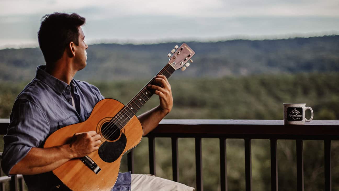 A man sitting on a balcony playing the guitar.